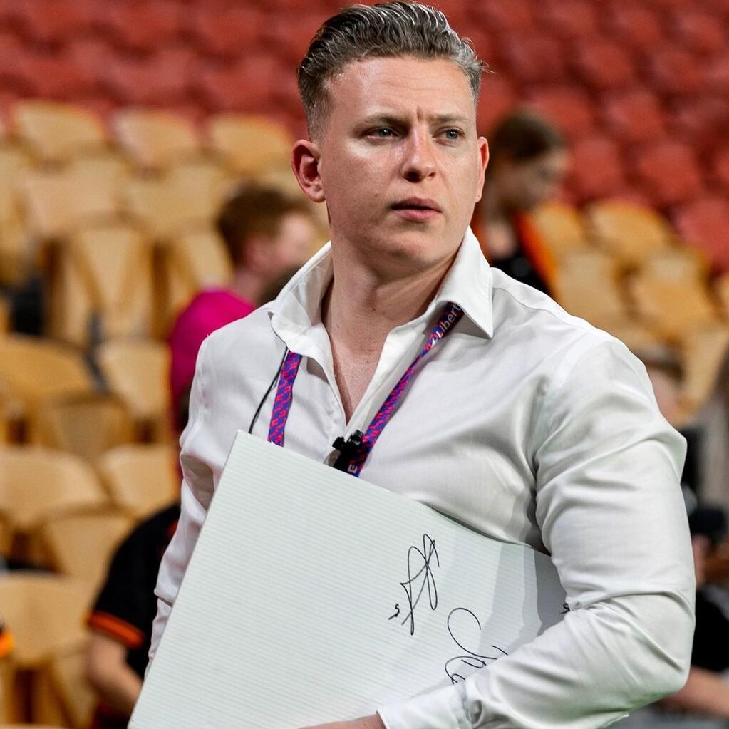 Sean Nicoll, Marketing Manager of Brisbane Roar, in a sports setting holding a clipboard, endorsing Jakob's video content and professionalism over a six-month collaboration with Unreal Media.