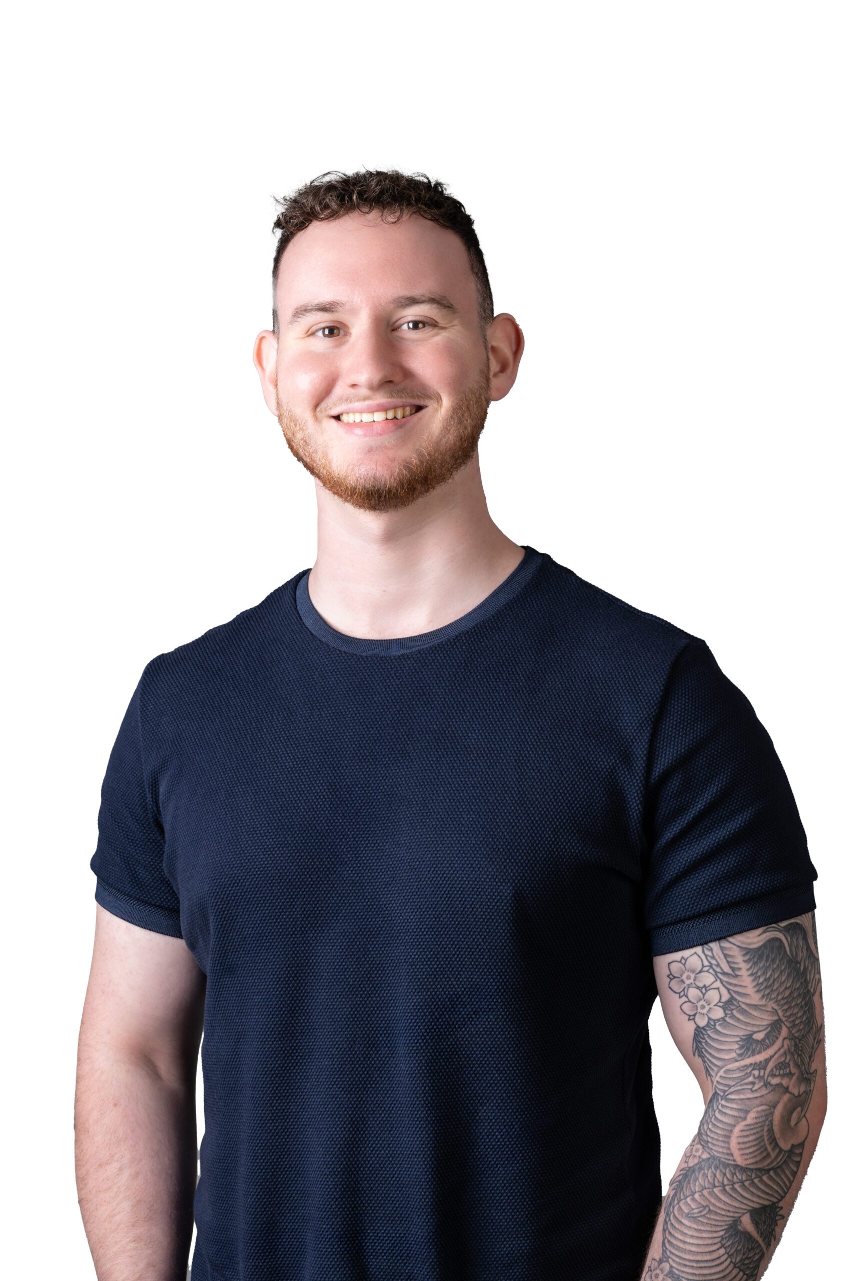 Smiling young entrepreneur with a short haircut and a sleeve tattoo standing against a black background, wearing a dark blue textured t-shirt, embodying a professional yet approachable image.