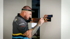 Smarter Air technician wearing a headlamp installs a wall-mounted air conditioning control panel, wiring exposed during the fit-out.