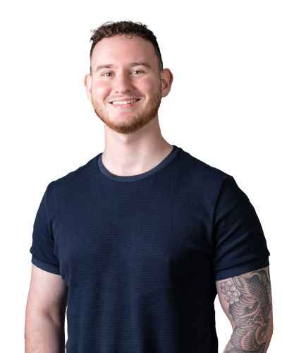 Smiling young entrepreneur with a short haircut and a sleeve tattoo standing against a black background, wearing a dark blue textured t-shirt, embodying a professional yet approachable image.